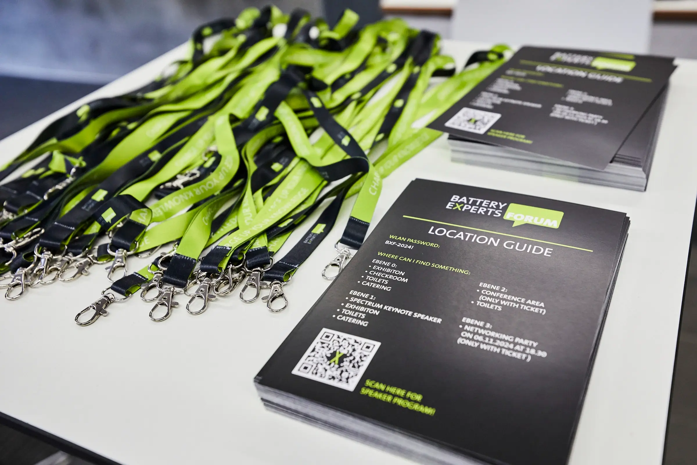 Lanyards, Programmflyer und Location Guides des Battery Experts Forum liegen auf einem Tisch bereit und zeigen das Corporate Design der Veranstaltung in Schwarz und Grün.
