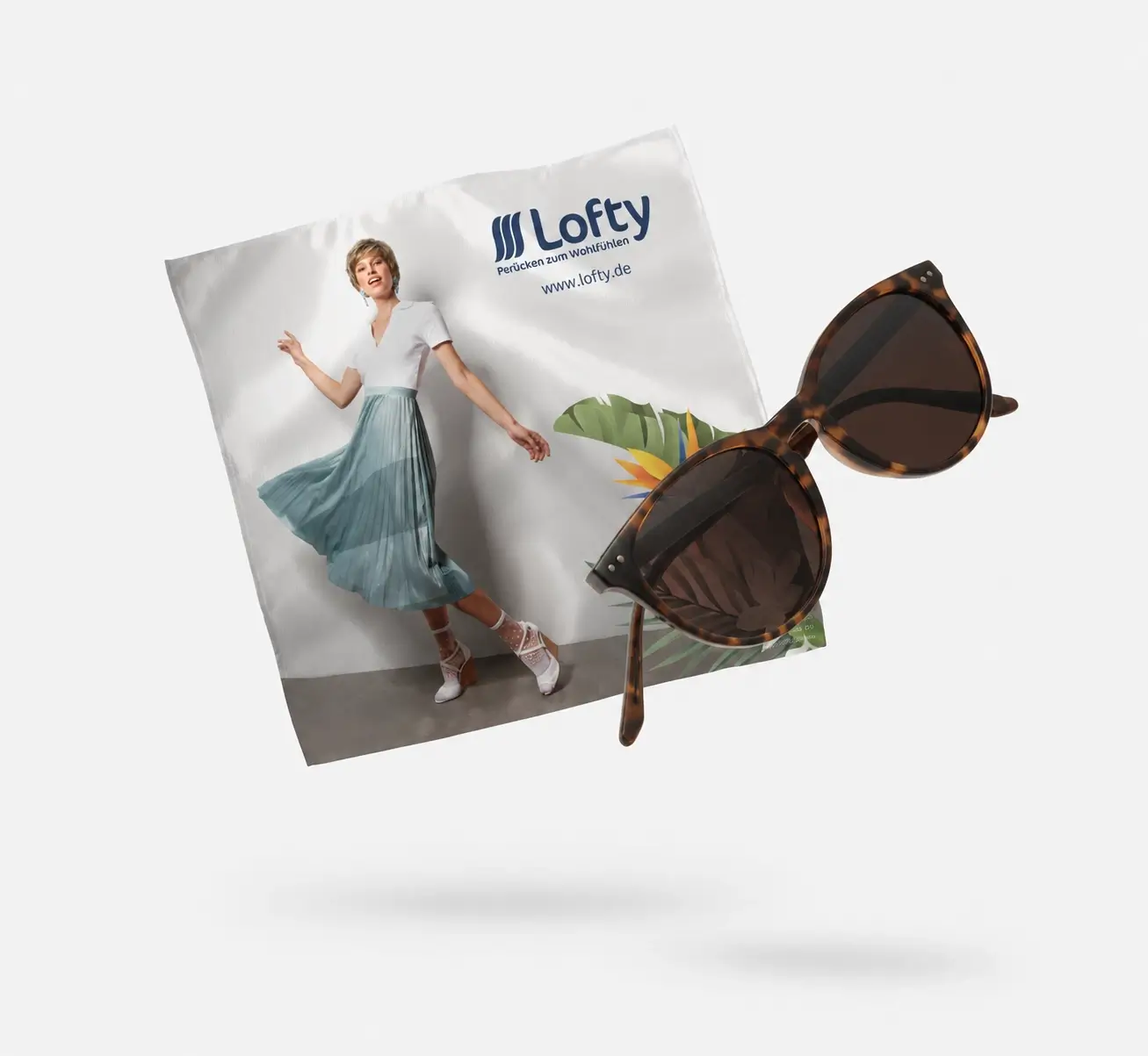 Schwebend inszeniertes Lofty-Brillenputztuch mit Modelmotiv und Logo, kombiniert mit einer Sonnenbrille in Schildpatt-Optik. Beide Elemente wirken durch Schatten und Perspektive leicht schwebend vor hellem Hintergrund.