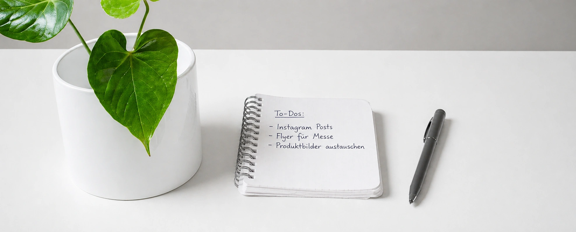 Schreibtisch mit Notizblock, Stift und Zimmerpflanze als Symbol für laufende Designunterstützung und alltägliche Marketingaufgaben.
